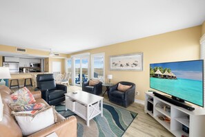 Uma sala de estar com televisão, sofás, mesa de centro e vista para o oceano.