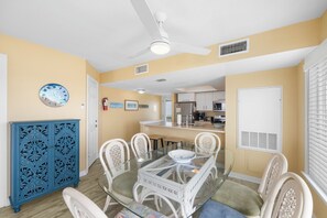 Uma sala de jantar com uma mesa de vidro, cadeiras brancas, um armário azul e um ventilador de teto.