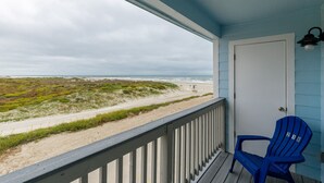 A beach view from a porch with a blue Adirondack chair and a door. - Spacious Beachside Escape | 3 Balconies, Gulf Views & Heated Pool (Corpus Christi)