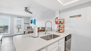 A modern kitchen with a large island, a built-in dishwasher, and a ceiling fan. - End Unit Beach Condo | Pool, Hot Tub & Scenic Dunes Views (Corpus Christi)