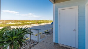 A building with a blue exterior, a white door, and a parking lot with a blue car. - End Unit Beach Condo | Pool, Hot Tub & Scenic Dunes Views (Corpus Christi)