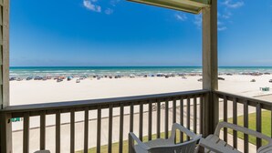A beach view from a covered balcony with chairs, a clear sky, and a sandy beach with parked cars. - Beachfront Escape | Heated Pool & Gulf Views (Corpus Christi)
