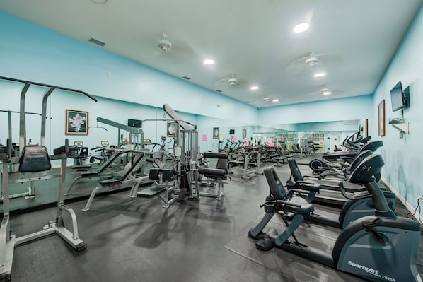 A gym with various exercise equipment, including treadmills and weight machines, and mirrors on the walls.