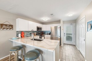 A kitchen with white cabinets, a large island with bar stools, stainless steel appliances, and a 'Beach' sign on the wall.