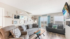 A living room with a grey sofa, a wooden coffee table, and a staircase leading to a balcony. - Beachside Family Escape | Balconies & Steps to Sand (Corpus Christi)