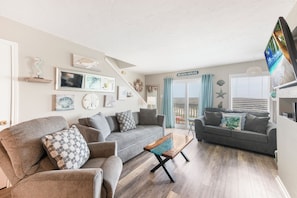 A living room with a grey sofa, a wooden coffee table, and a staircase leading to a balcony.