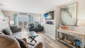 A living room with a sofa, a coffee table, a TV, and a console table with decorative items. - Beachside Family Escape | Balconies & Steps to Sand (Corpus Christi)