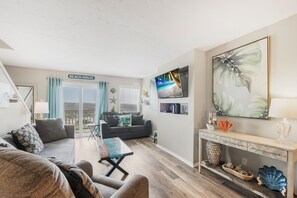 Un salon comprenant un canapé, une table basse, un téléviseur et une console sur laquelle sont disposés des objets décoratifs.
