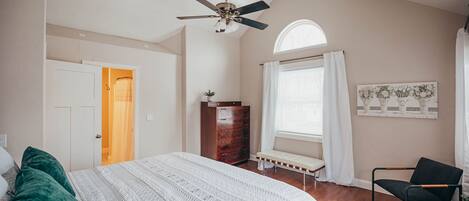 A bedroom with a bed, a dresser, a bench, a chair, a ceiling fan, and a window with curtains.