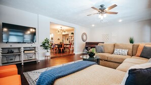 A modern living room with a flat-screen TV, a ceiling fan, a sofa, and a dining area in the background. - 6 bedroom Large house in Pickwick district Springfield Near MSU (Springfield)