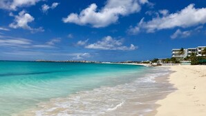 A beach with clear turquoise water, a sandy shore, and a row of buildings with balconies.