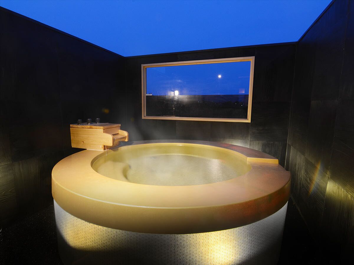 Un bain à remous doté d’un banc en bois, d’une étagère en bois et offrant une vue encadrée sur le ciel nocturne.