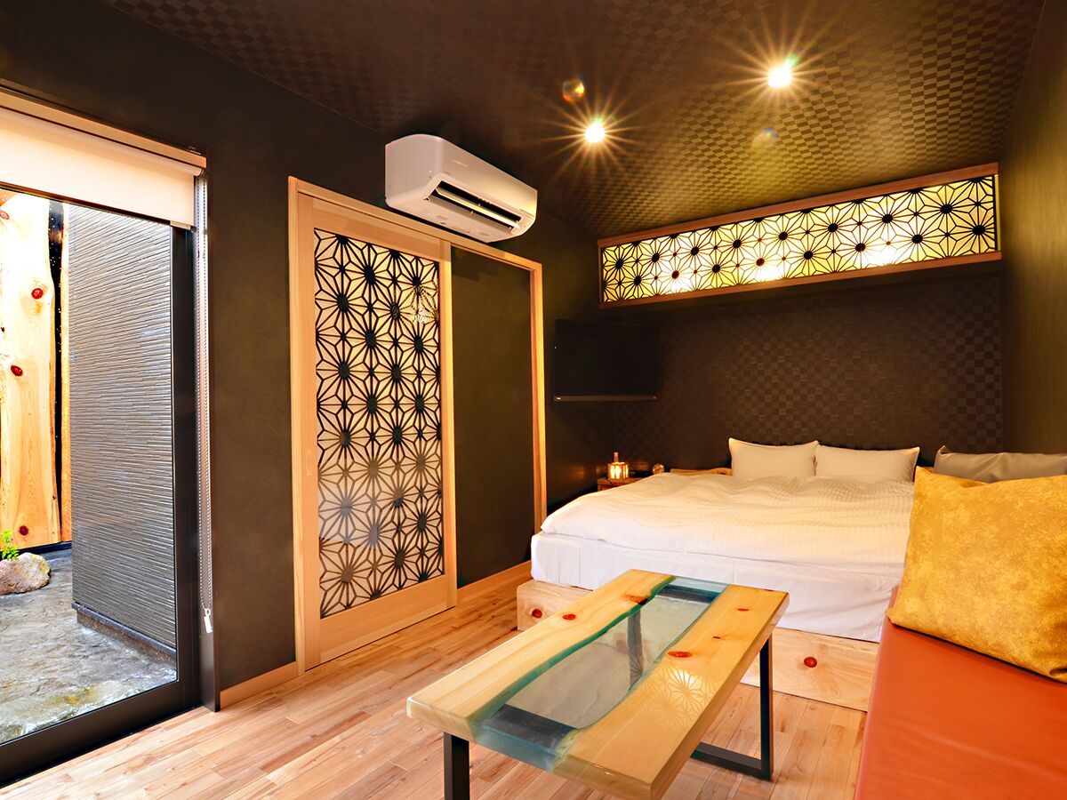 A modern hotel room with a bed, a glass coffee table, a decorative screen, and an air conditioning unit.
