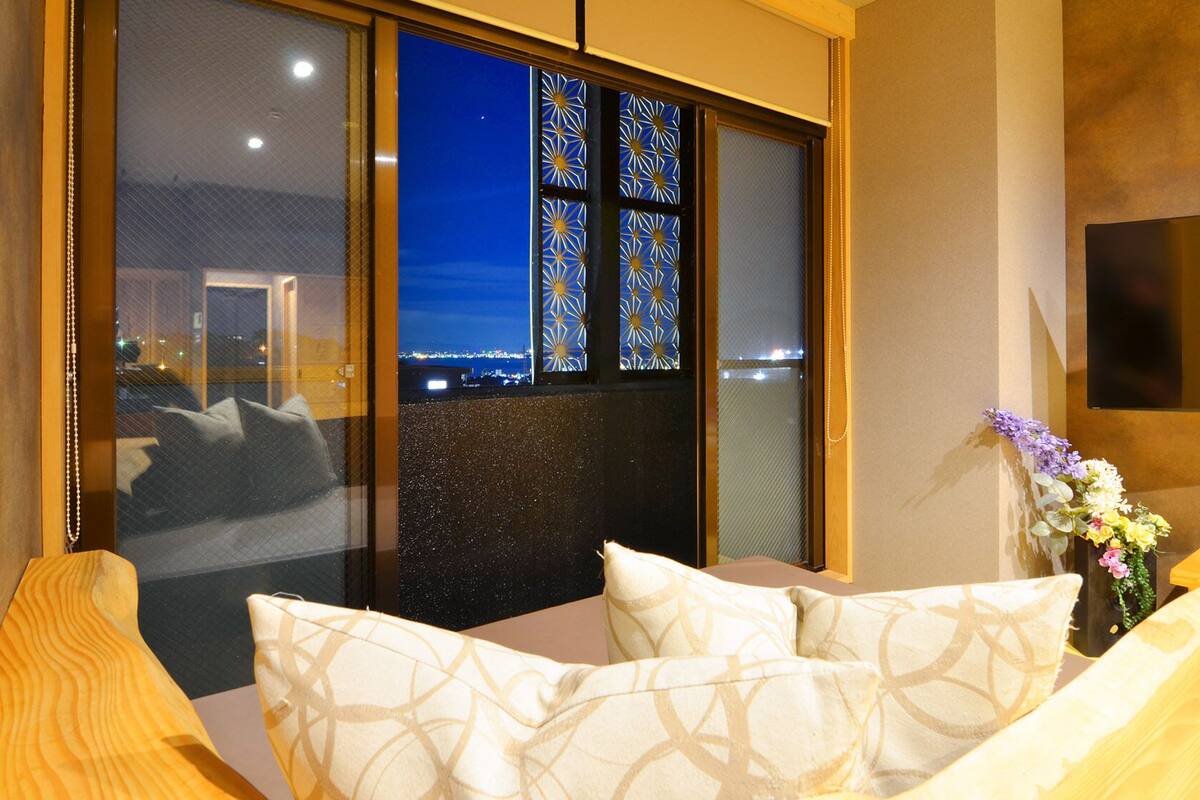 Ein modernes Zimmer mit einem großen Fenster, einem Flachbildfernseher und einem Sofa mit gemusterten Kissen.