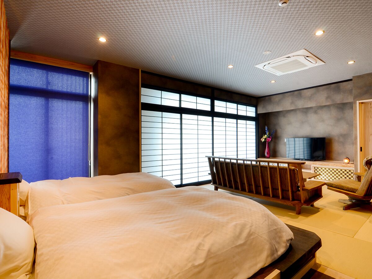 A hotel room with two beds, a TV, a seating area, and large windows.