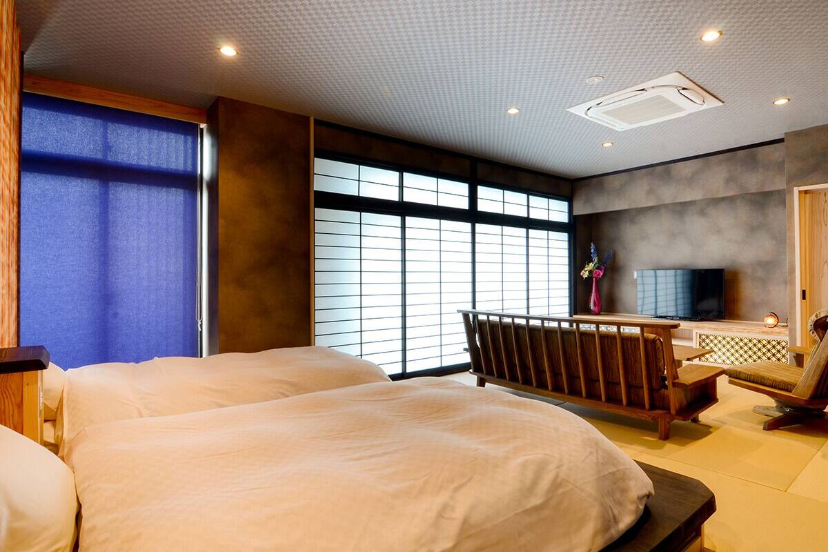 Ein Hotelzimmer mit zwei Betten, einem Fernseher, einer Sitzecke und großen Fenstern.