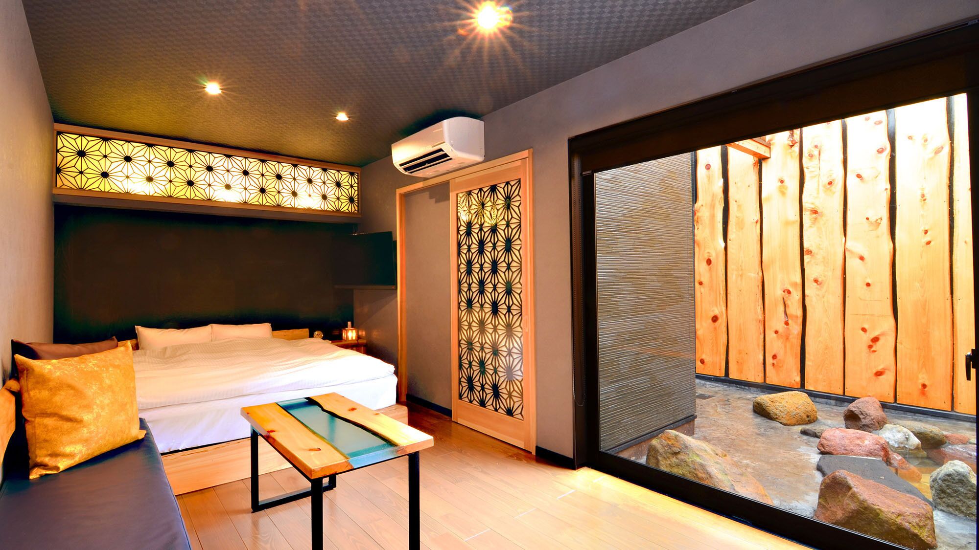 A bedroom with a bed, bedside table, and a view of a wooden deck through a sliding glass door.