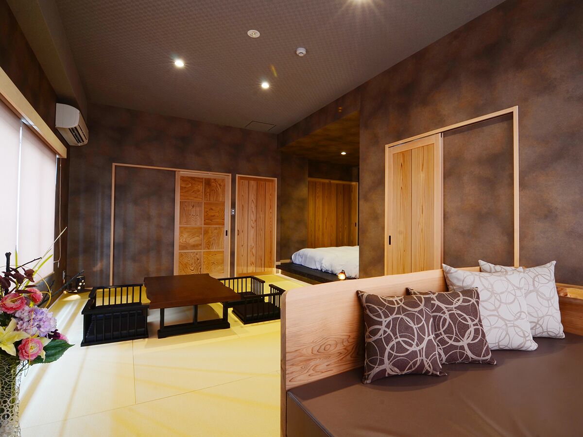 A room with a bed, a small table, a bench, and a wall-mounted heater.