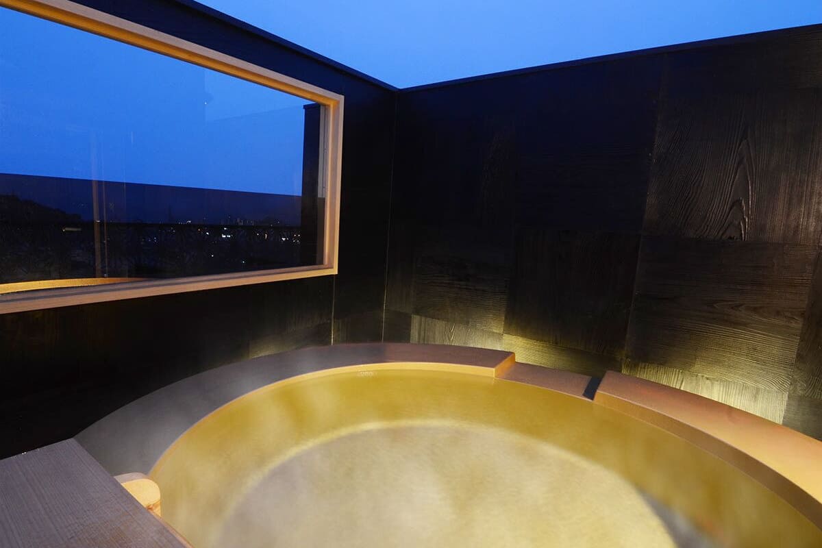 A hot tub in a room with a window overlooking a cityscape at dusk.