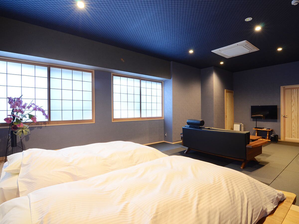 A hotel room with two beds, a sofa, a TV, and large windows.