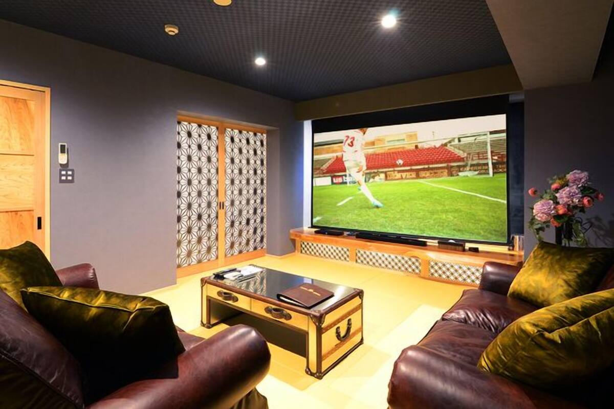 Ein Wohnzimmer mit großem Flachbildfernseher, Ledersofas, einem Couchtisch und einer dekorativen Wandverkleidung.