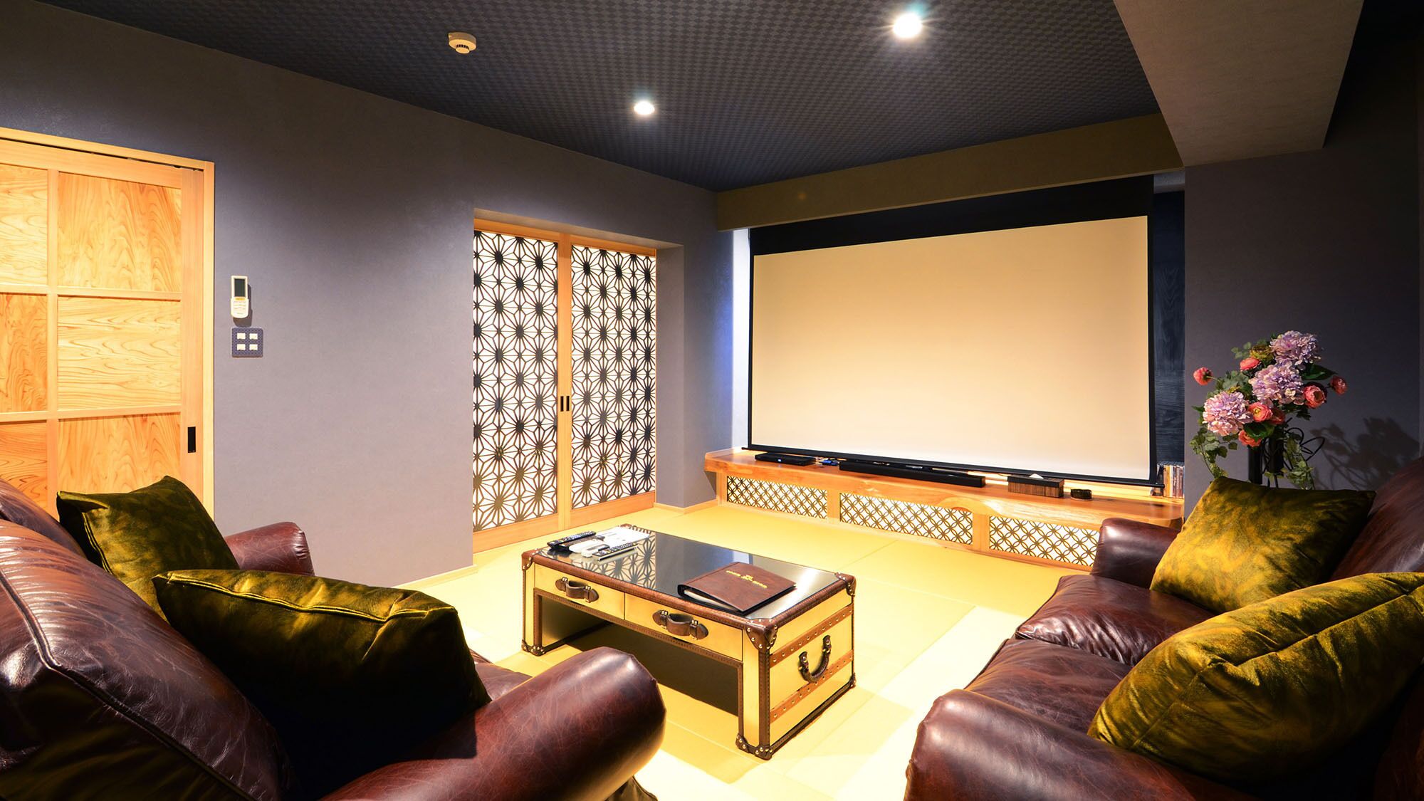 Une salle de cinéma maison avec des canapés en cuir, une table basse en verre, un grand téléviseur à écran plat et une porte décorative.