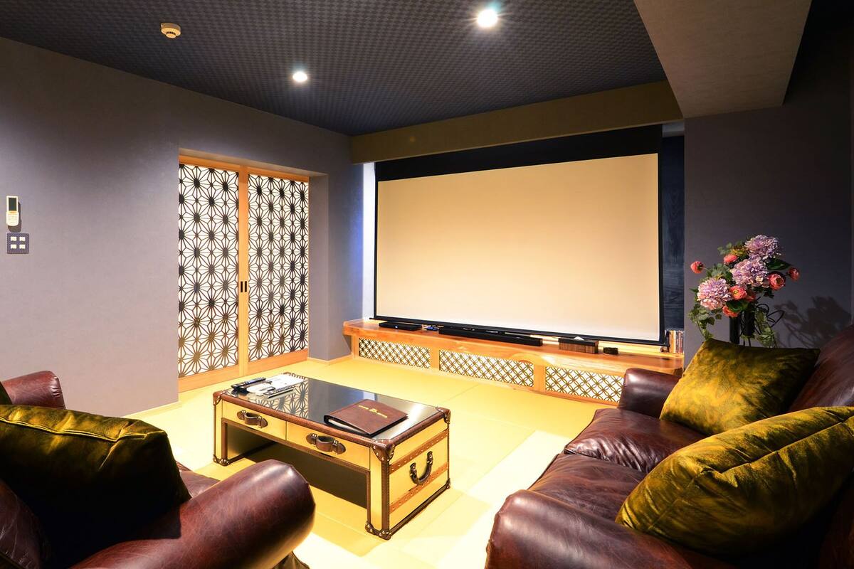 Ein Heimkinozimmer mit Ledersofas, einem Glastisch, einem großen Flachbildfernseher und einer dekorativen Raumtür.