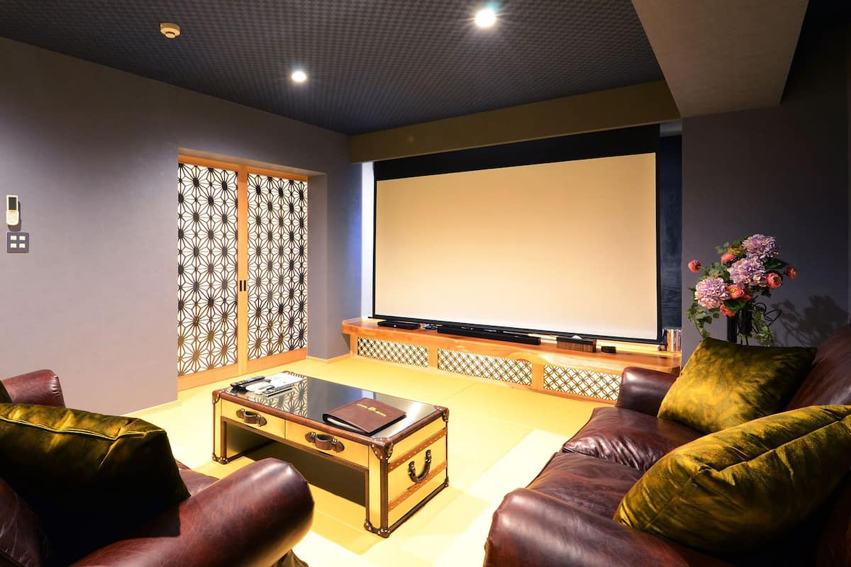 Una sala de cine en casa con sofás de cuero, una mesa de centro de vidrio, un televisor de pantalla plana grande y un portón decorativo.