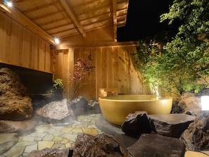 Un espace de détente en bois avec un jacuzzi entouré de rochers et un sol en pierre.