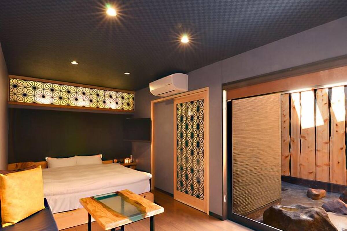 Ein modernes Hotelzimmer mit einem Bett, einem kleinen Tisch, einer Wand mit Dekoration und einer Schiebetür zu einem Badezimmer.