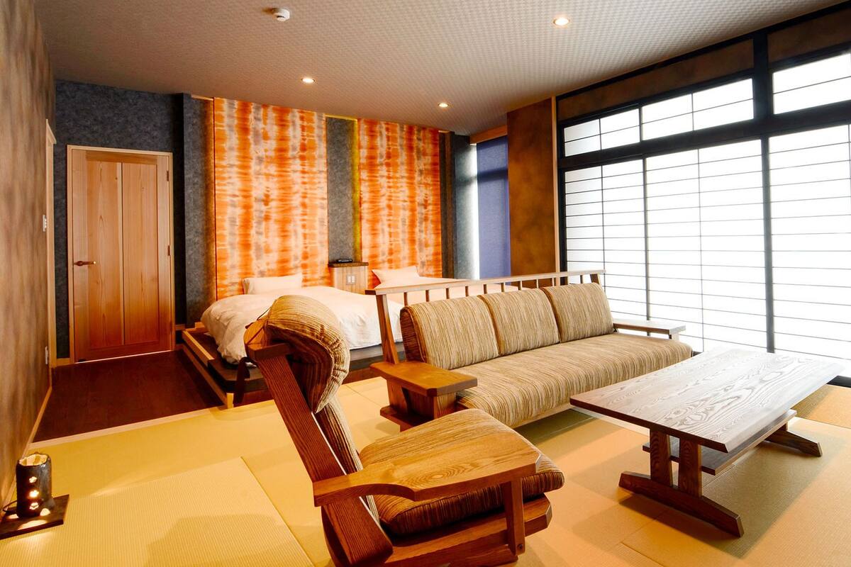 Ein Zimmer mit Bett, Schlafsofa, Holzmöbeln und großen Fenstern.