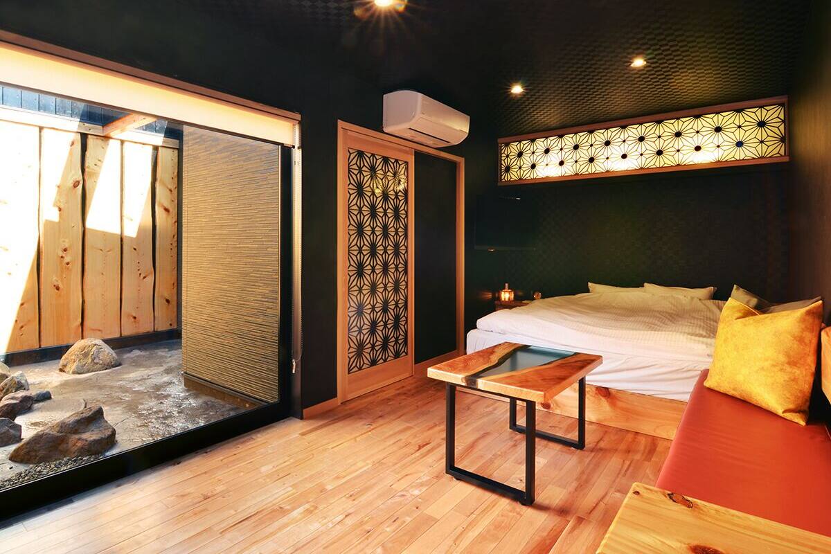 Ein Zimmer mit einem Bett, einem Holztisch, einem dekorativen Raumteiler und einer kleinen Wasserspülung.