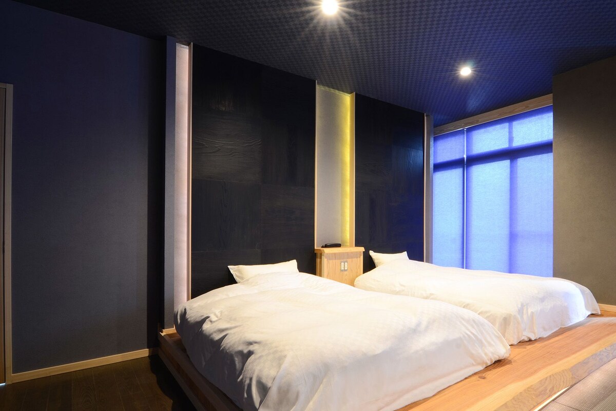 A hotel room with two beds, a small wooden nightstand, and a large window with blinds.