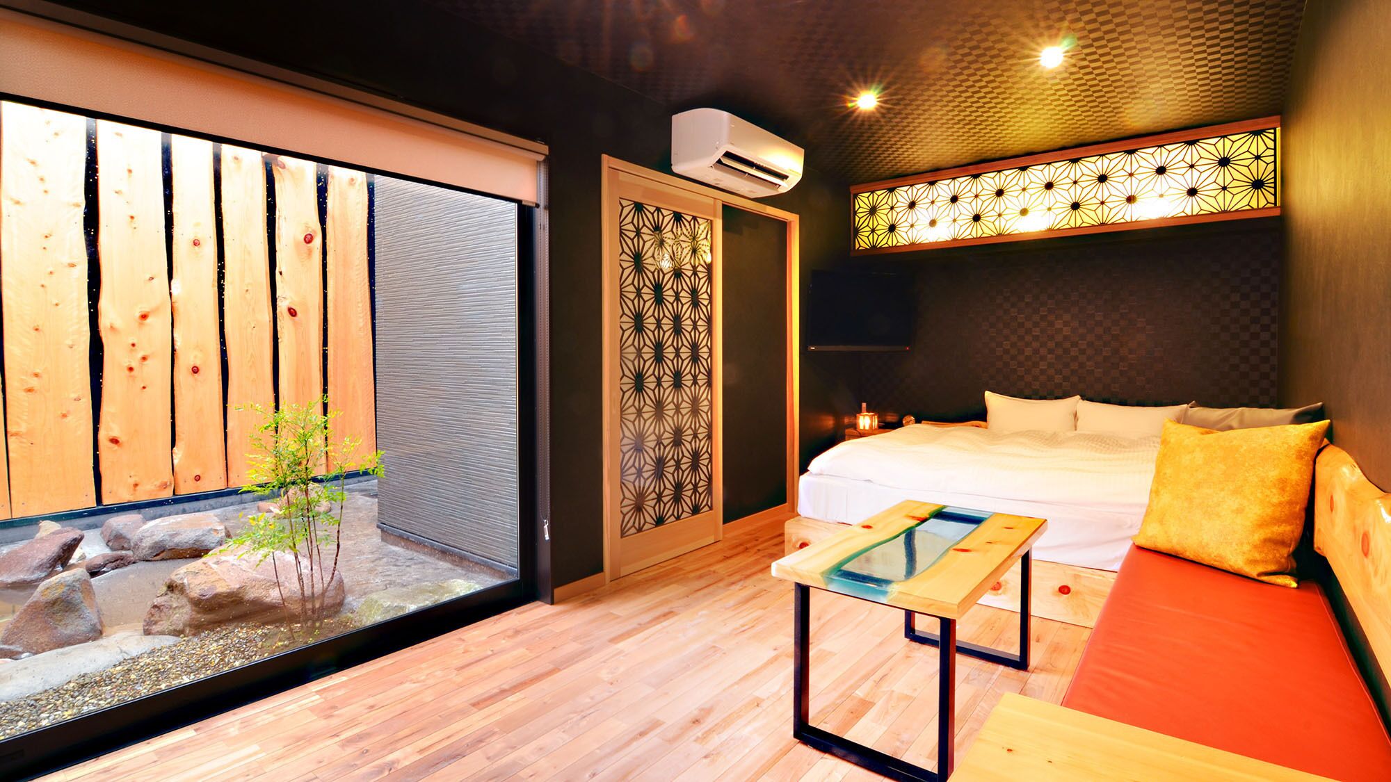 A modern bedroom with a bed, a small table, a window with a view of wooden planks, and an air conditioning unit.
