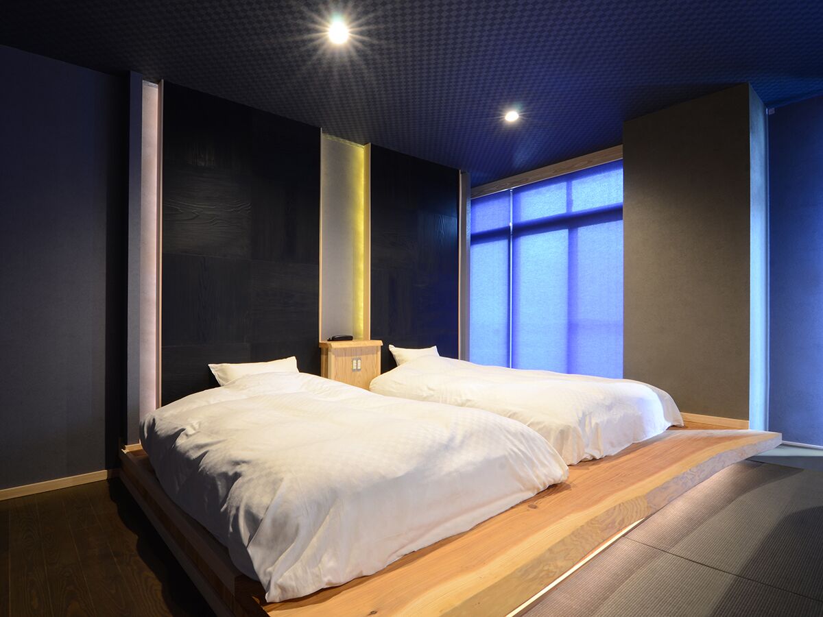 A double bed with white linens, a wooden floor, and a large window with blue-tinted glass.
