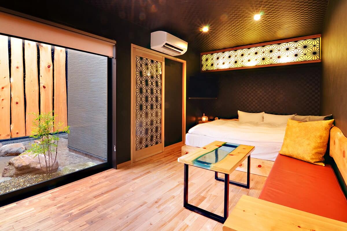 Ein modernes Hotelzimmer mit Bett, Holzboden, kleinem Tisch, Sofa und einer dekorativen Wandverkleidung.