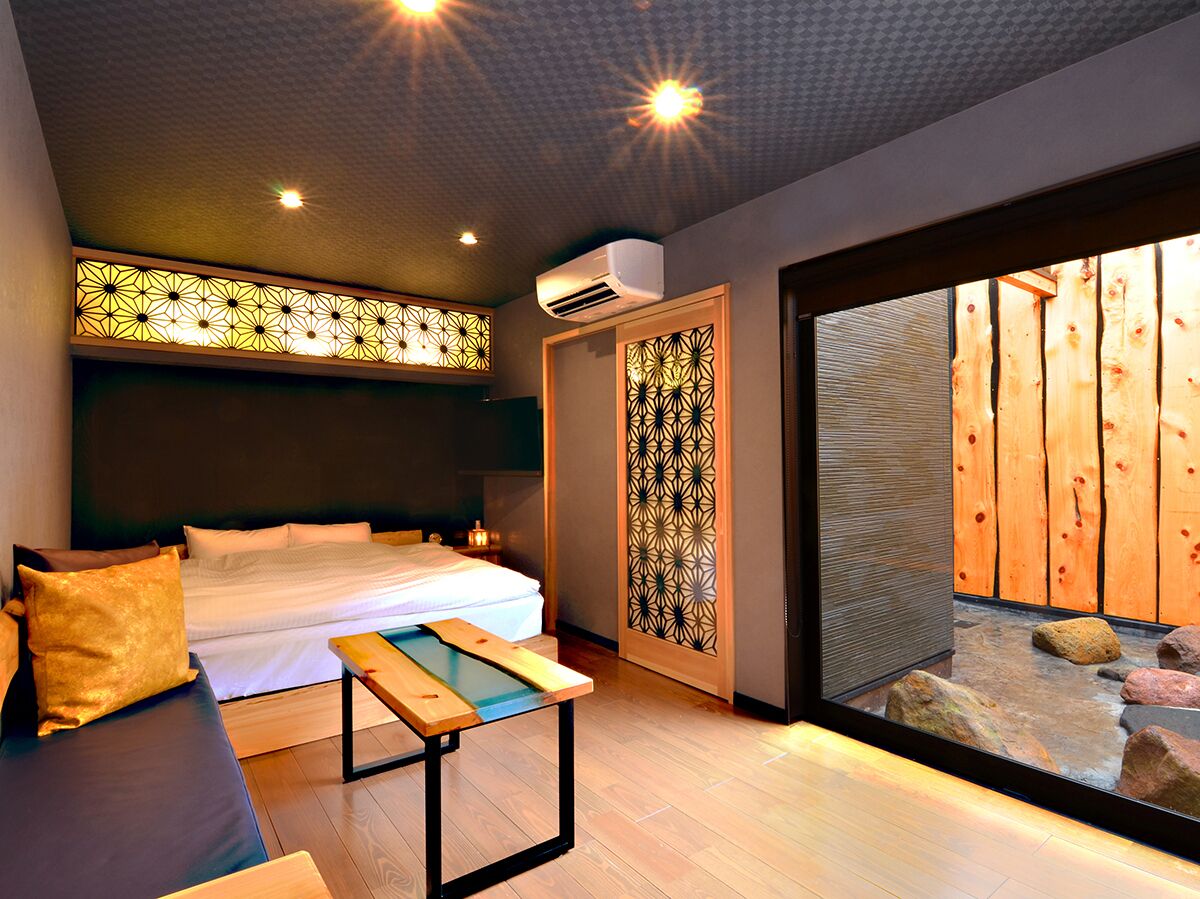A modern bedroom with a bed, bedside table, and a view of a wooden fence through a glass door.