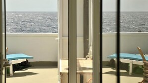Een balkon met uitzicht op de oceaan, twee blauwe tafels en een witte stoel.