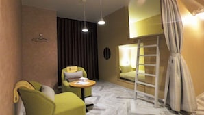 A hotel room with a bed, a chair, a small table, a mirror, a curtain, and a hanging light fixture. - Good Bless Garden Sauna Stay (Yonago)