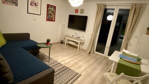 Una sala de estar con un sofá, un televisor, una mesita y una silla.