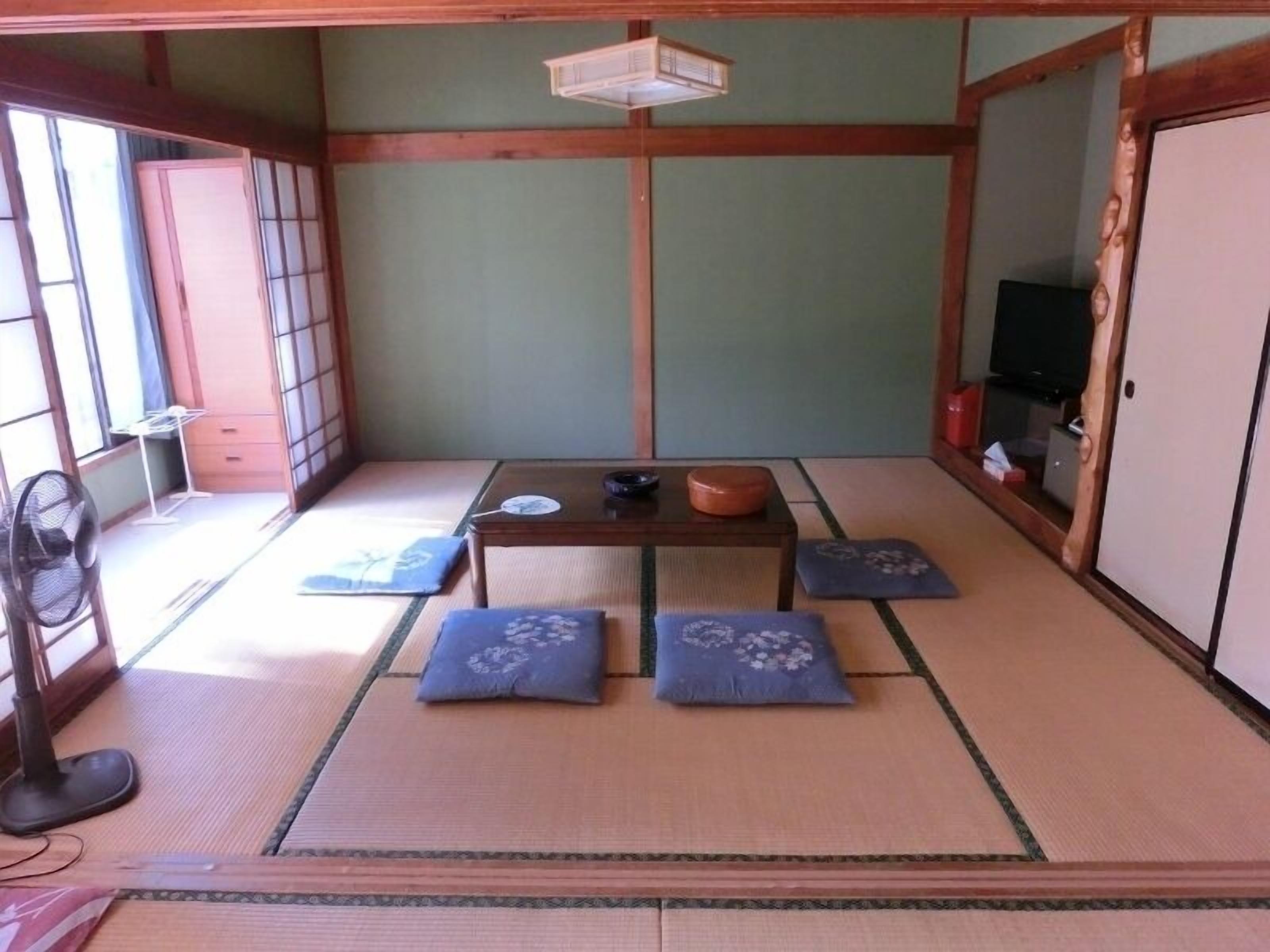 Una habitación japonesa tradicional con suelo de tatami, una mesa baja, cojines, un abanico y un televisor.