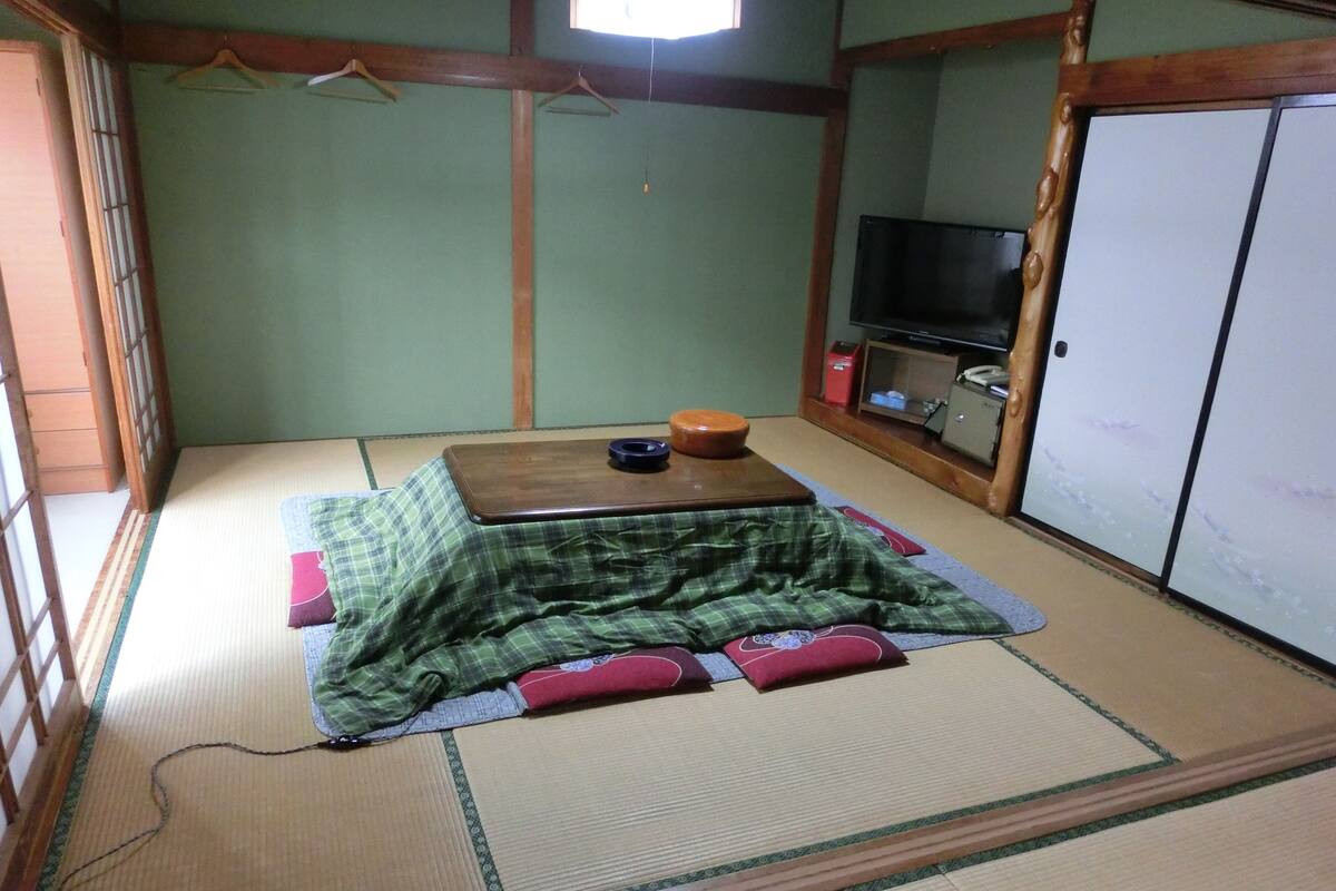 A tatami mat room with a futon bed, a small wooden table, a television, and a wardrobe.