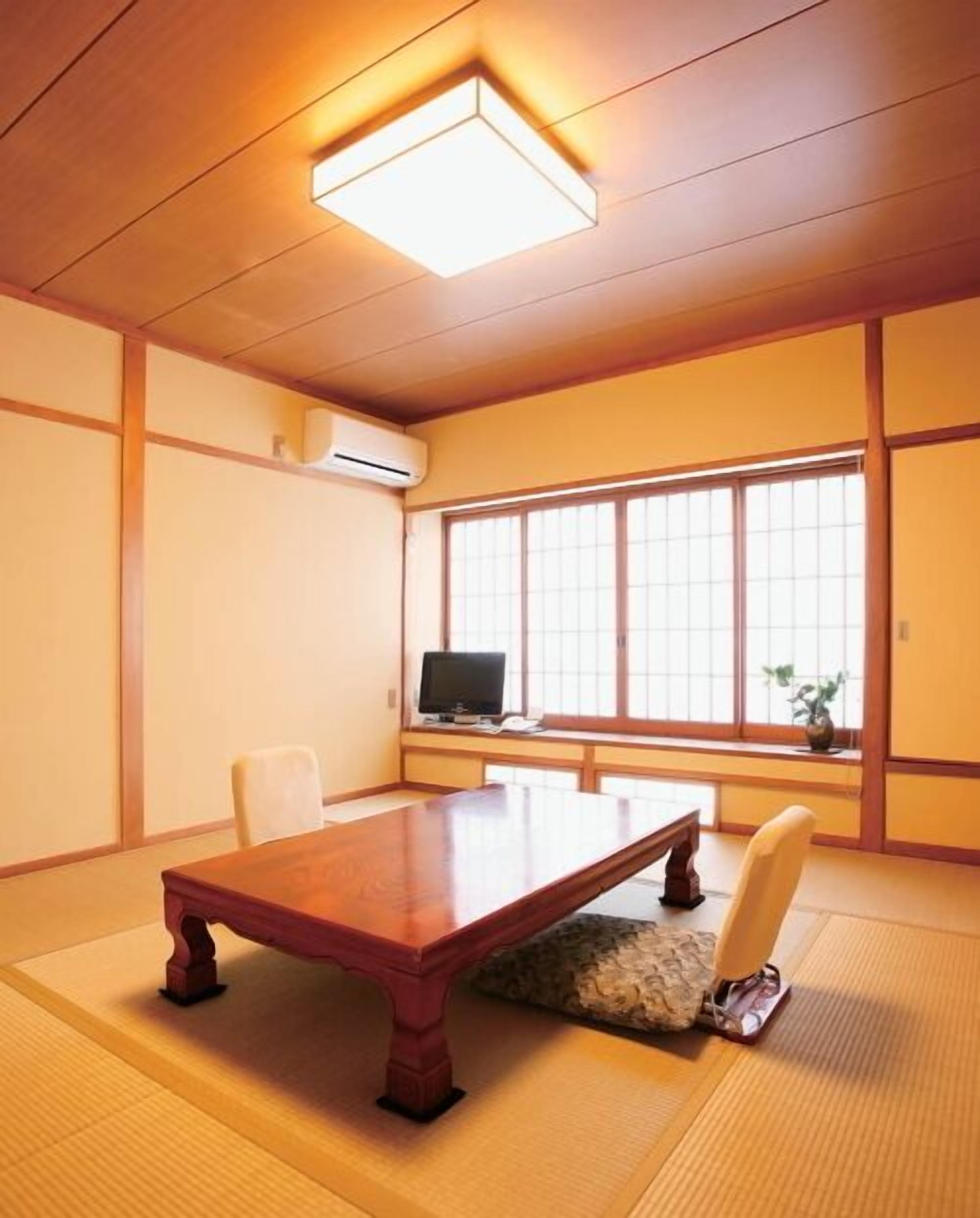 A traditional Japanese room with tatami flooring, a low wooden table, a television, and a sliding door.