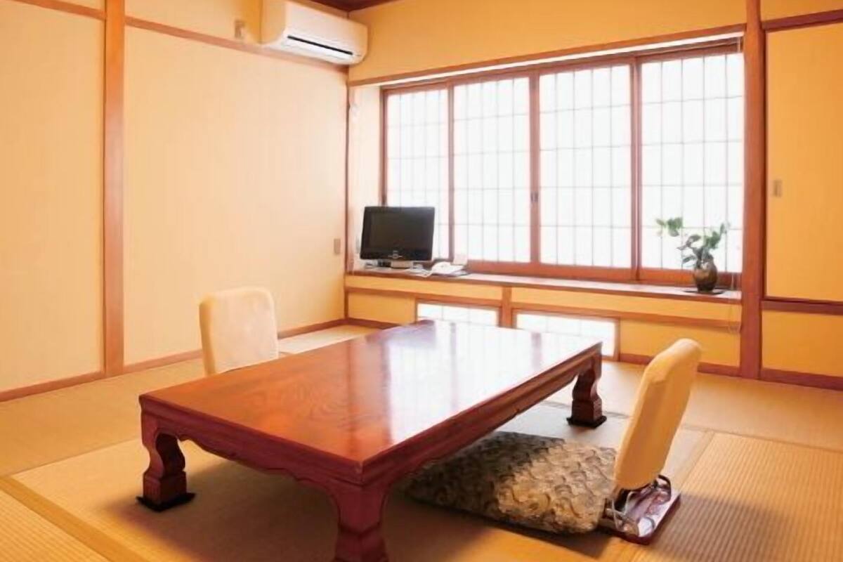 Een traditionele Japanse kamer met tatami vloerbedekking, een lage houten tafel, een televisie en een schuifdeur.