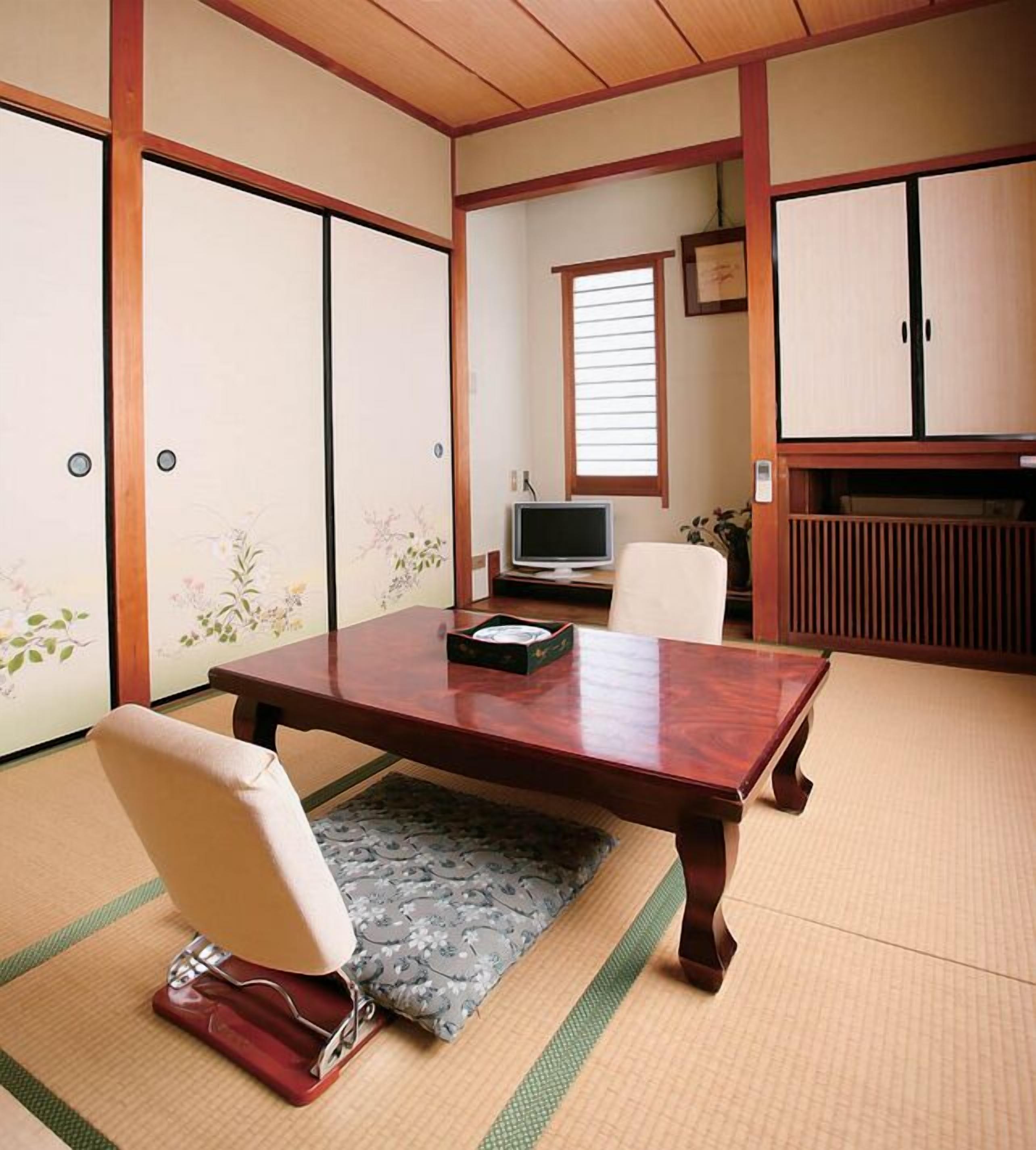A traditional Japanese room with tatami flooring, a low table, a chair, a television, and sliding doors.