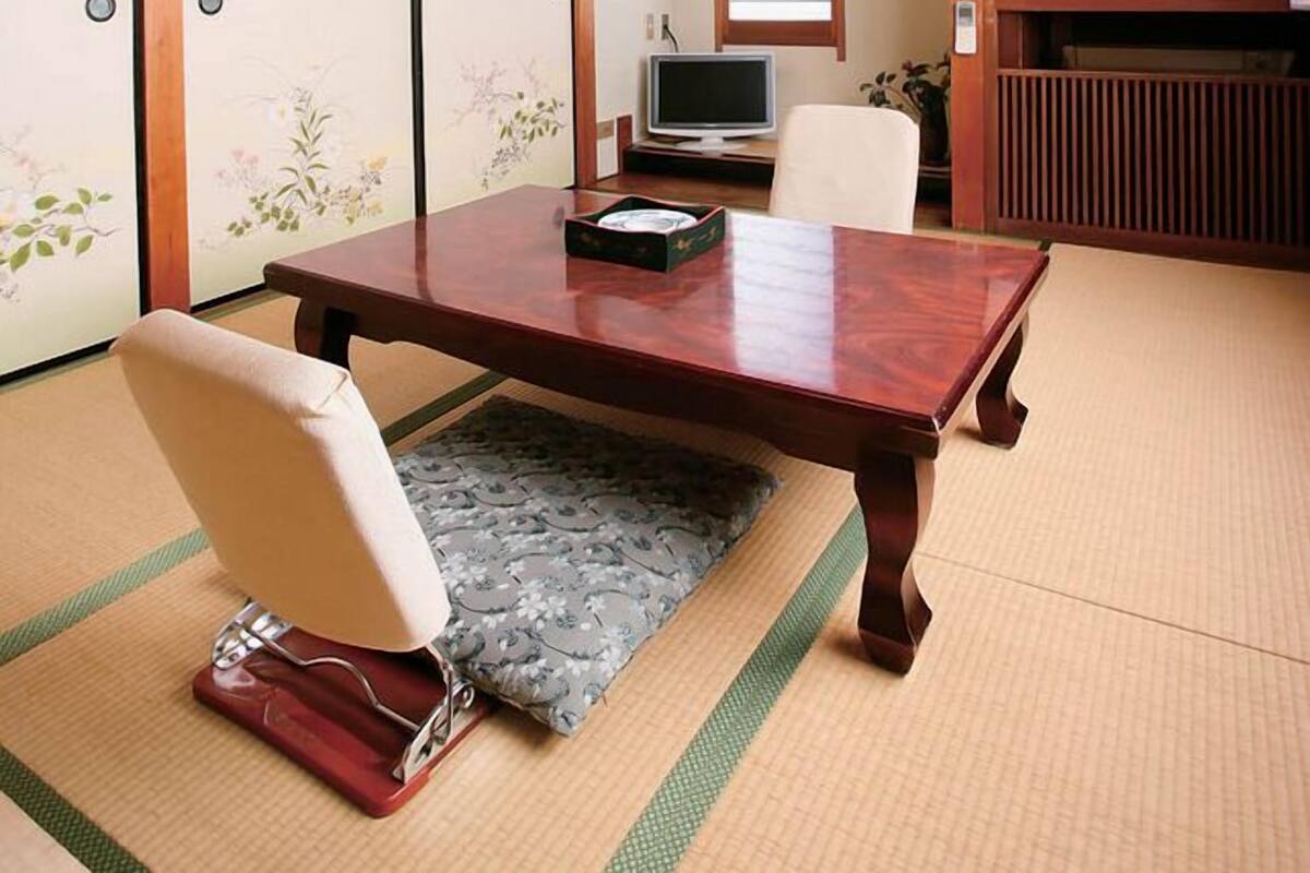 Een traditionele Japanse kamer met tatami vloerbedekking, een lage tafel, een stoel, een televisie en schuifdeuren.