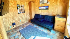 A room with a blue sofa, a small wooden cabinet, and a mounted air conditioner. - Mini Cowboy Cabin (Belfield)