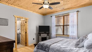 Un dormitorio con cama, televisión, chimenea y ventilador de techo.