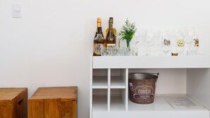 Una consola blanca con un espejo, botellas, vasos y un balde con la etiqueta 'CERVEJA TRADICIONAL'.