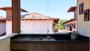Una cocina con un lavamanos, armarios de madera y una ventana con vistas a una calle con edificios.